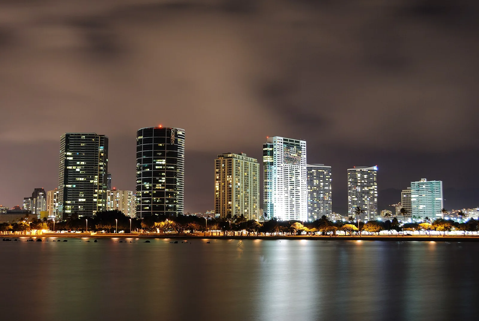 Lit condominium towers of Ala Moana and Kakaako reflected in the water at night