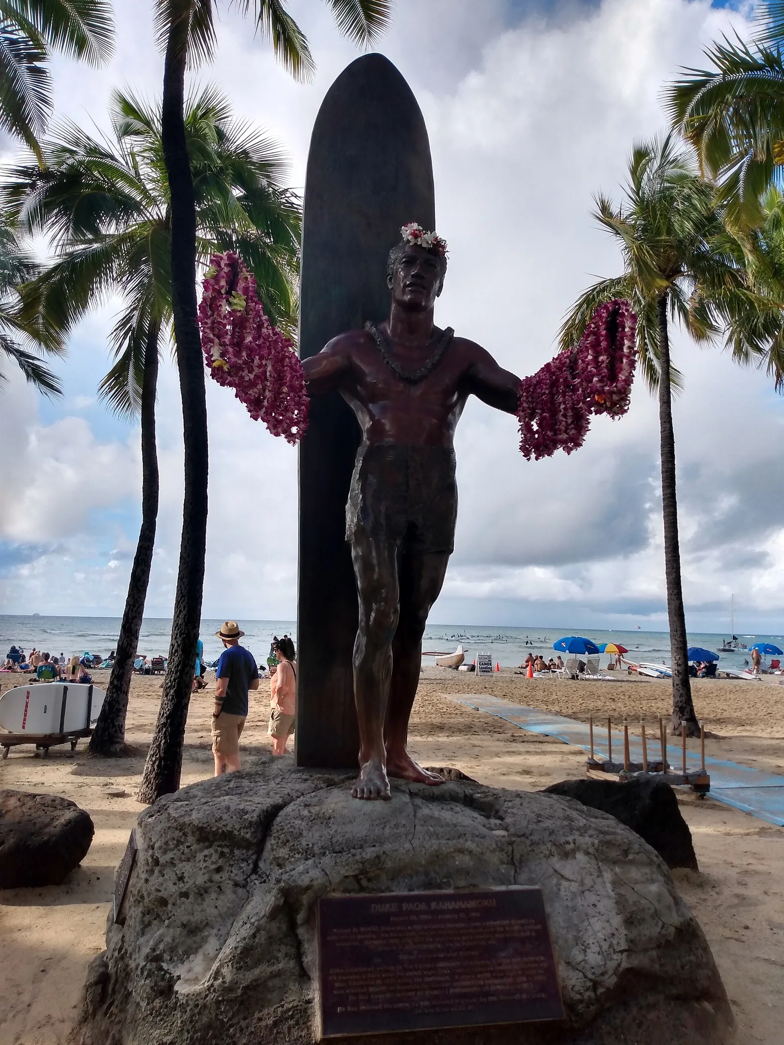 Bronze statue of Duke Kahanamoku with outstretched arms draped in lei, a surfboard behind him