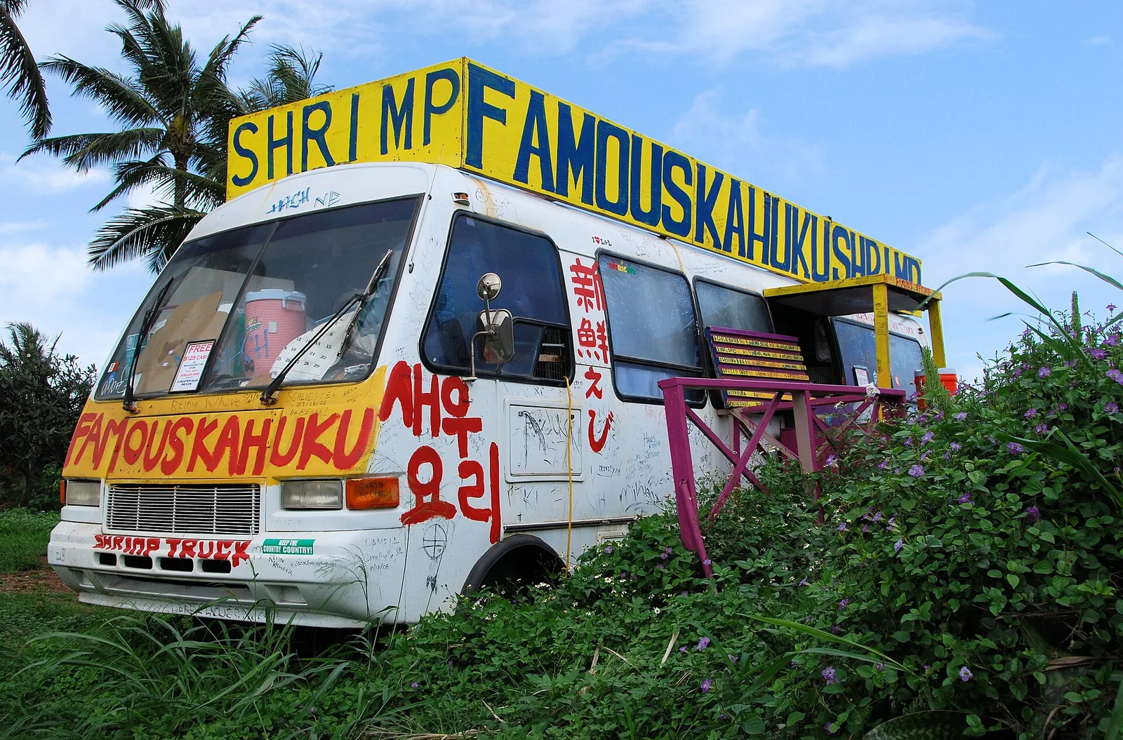 The graffiti-covered Famous Kahuku Shrimp truck parked under palm trees