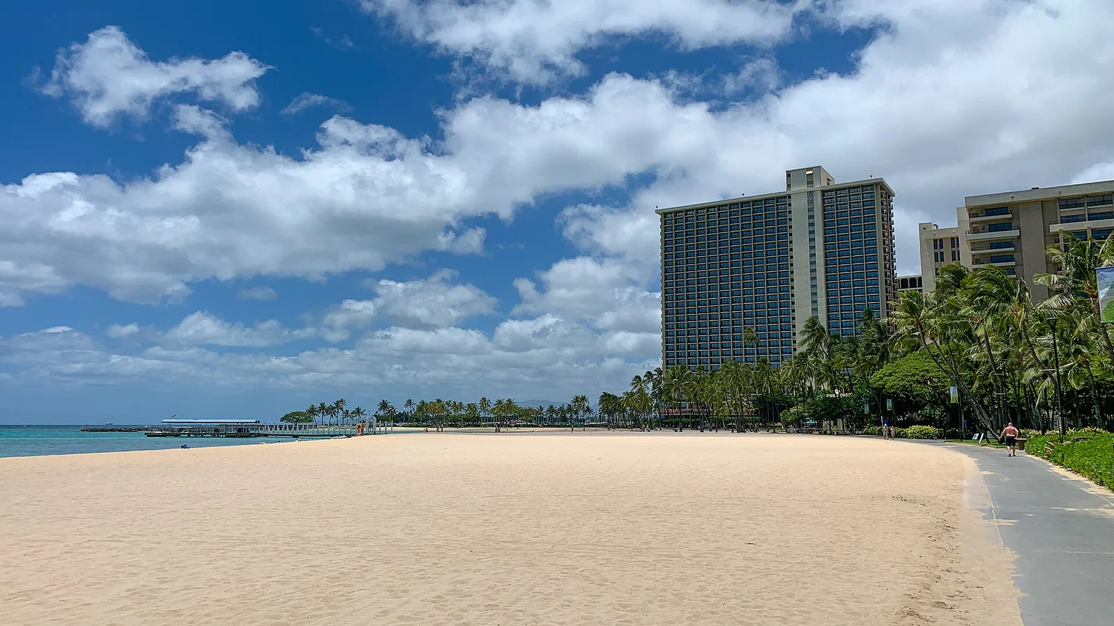The wide, empty sand of Fort DeRussy Beach with hotel towers and palms behind it