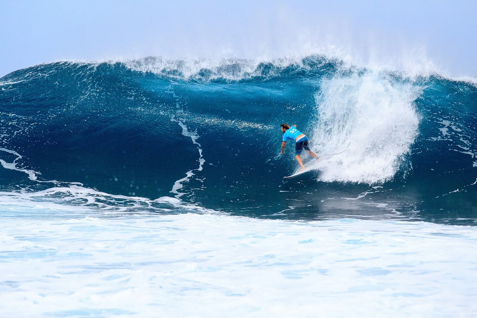 A surfer racing along the face of a large, hollow blue wave