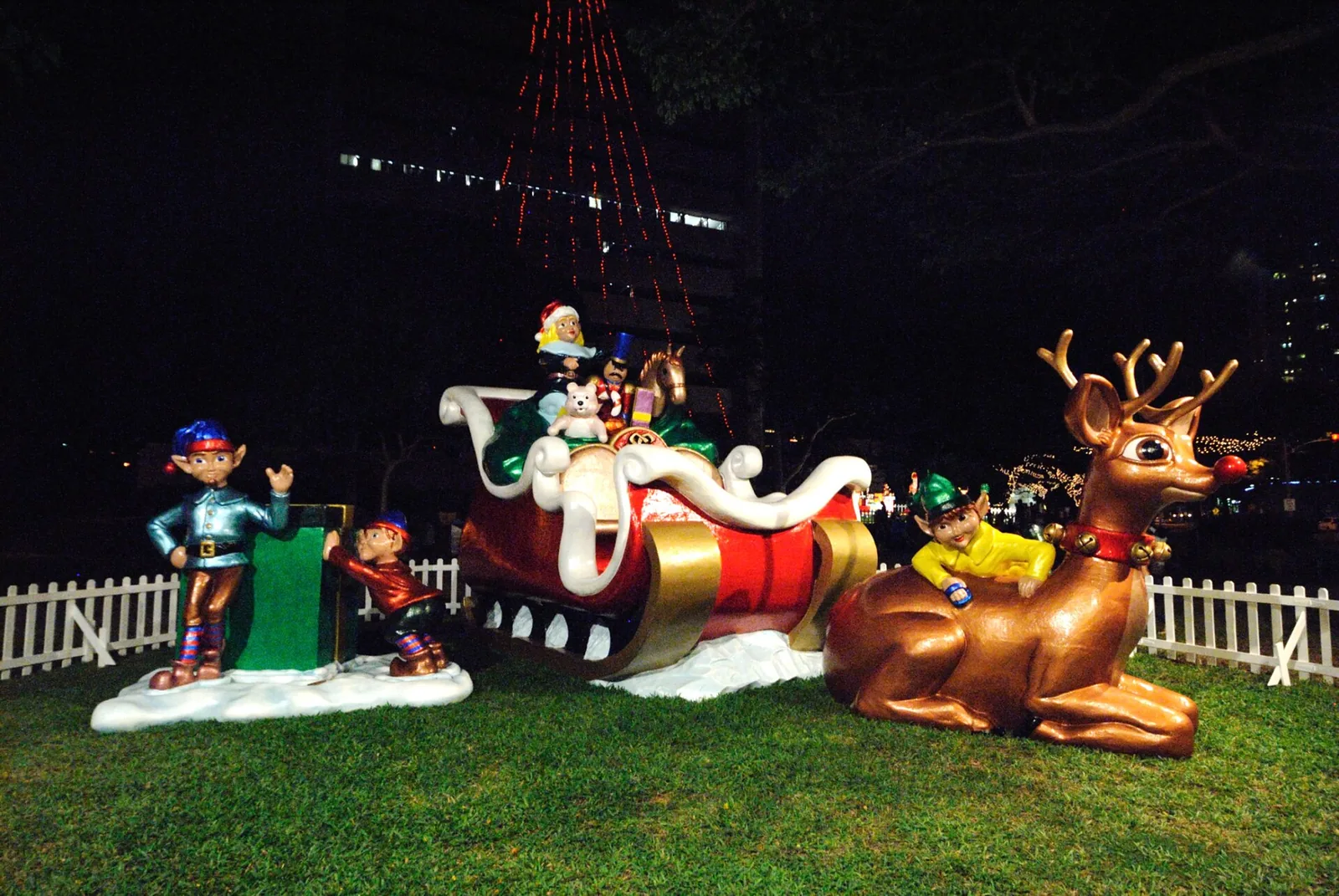 A Christmas sleigh with reindeer and elf figures lit up at night for Honolulu City Lights