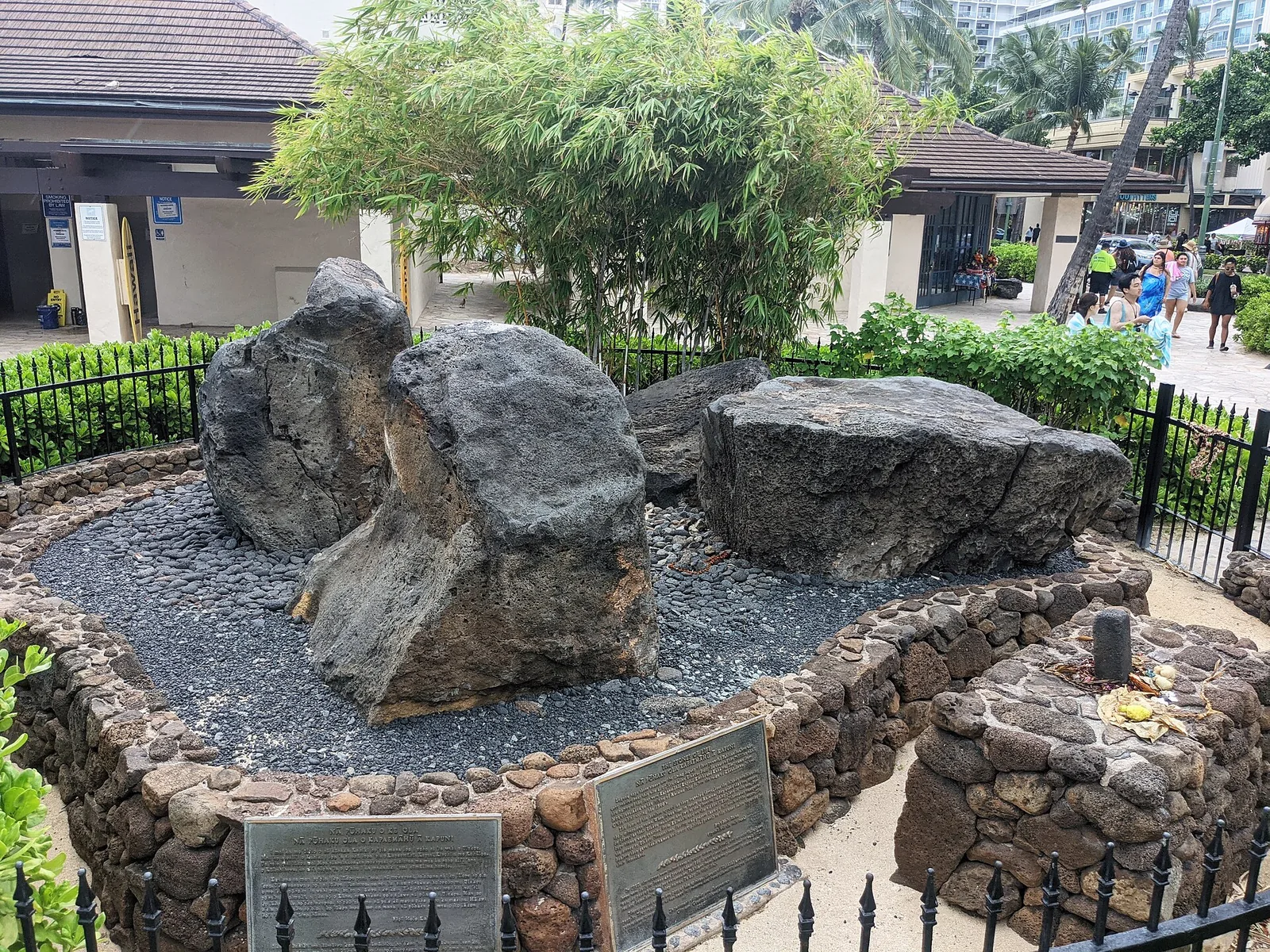 Four large basalt boulders inside a low stone wall and iron railing beside the beach promenade