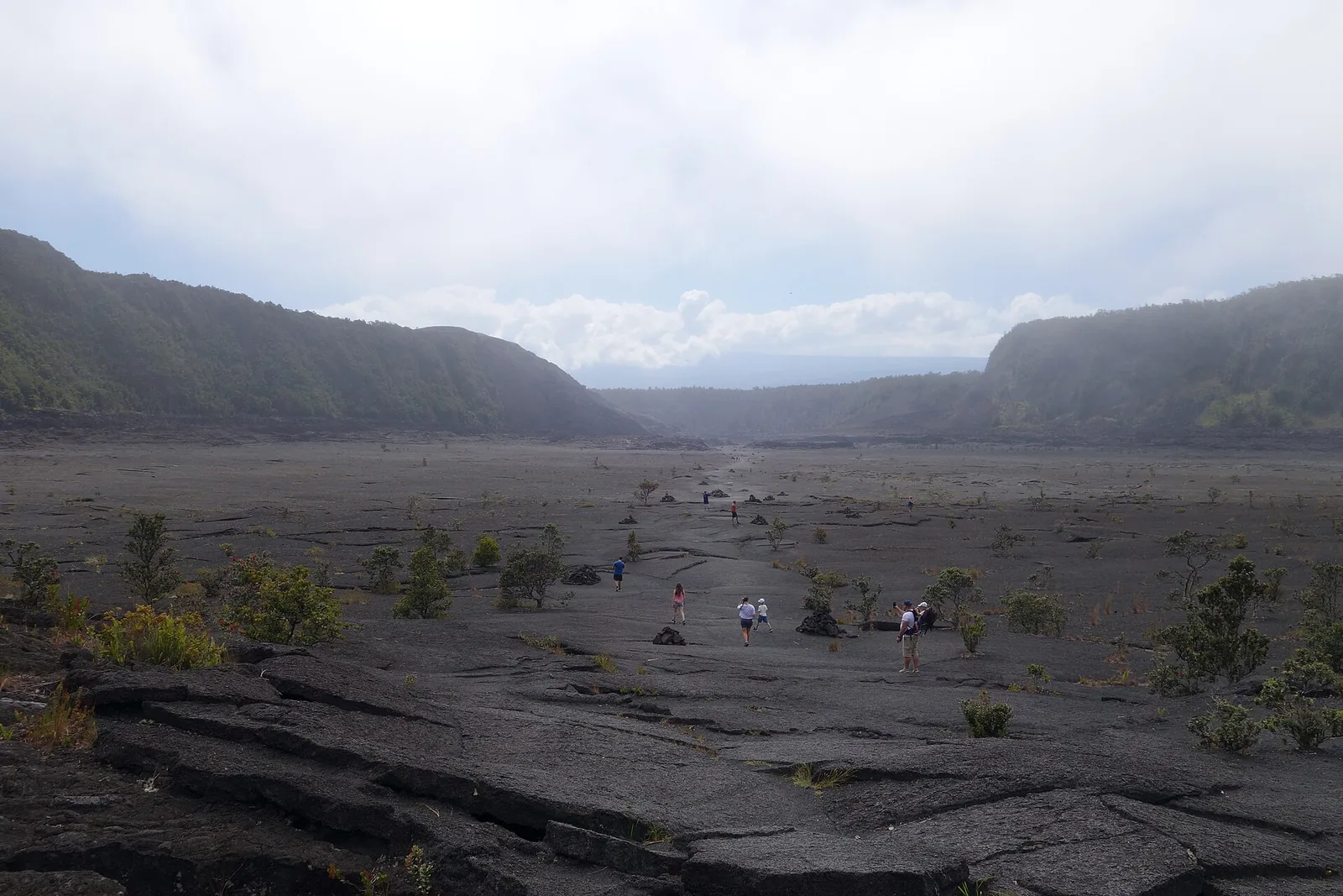 Hikers crossing the grey lava floor of Kilauea Iki crater in Hawaii Volcanoes National Park