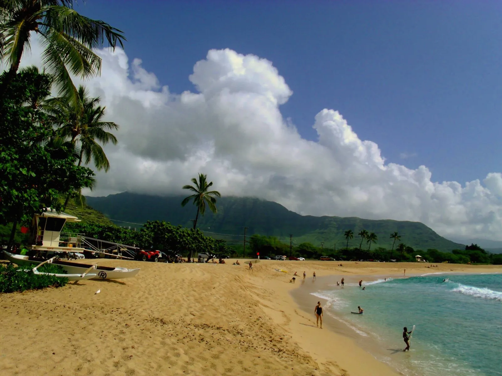A lifeguard tower on the wide sand of Makaha Beach Park beneath green mountains and clouds