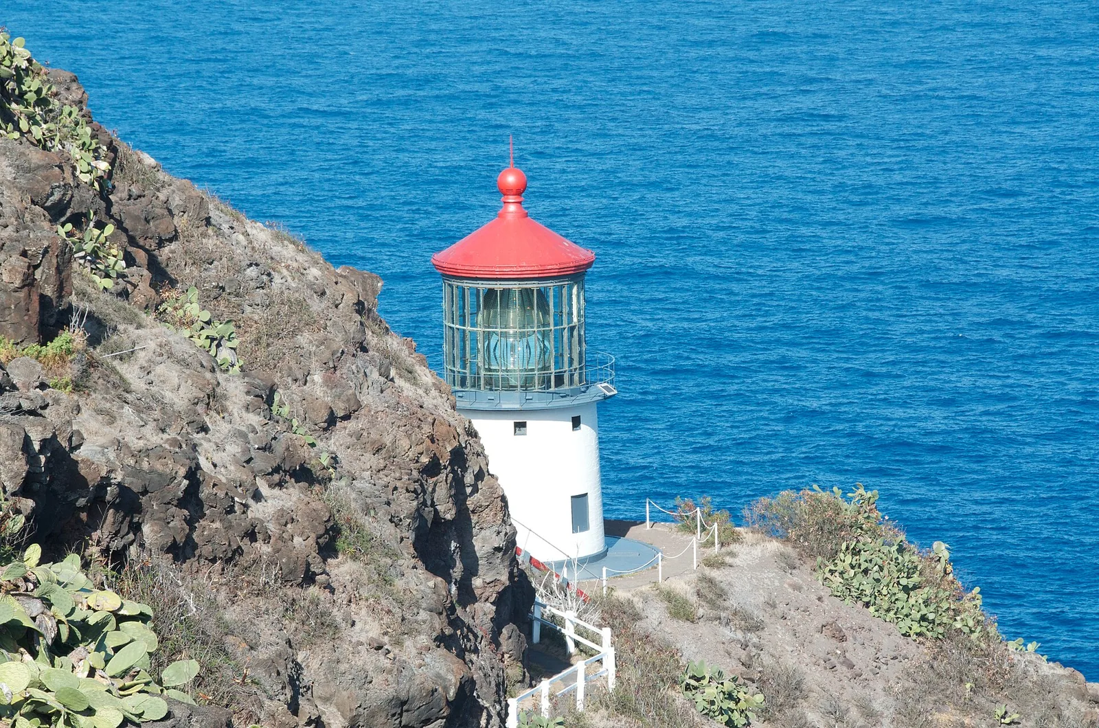 Makapuu Point Lighthouse with its red roof on a lava cliff above the deep blue Pacific