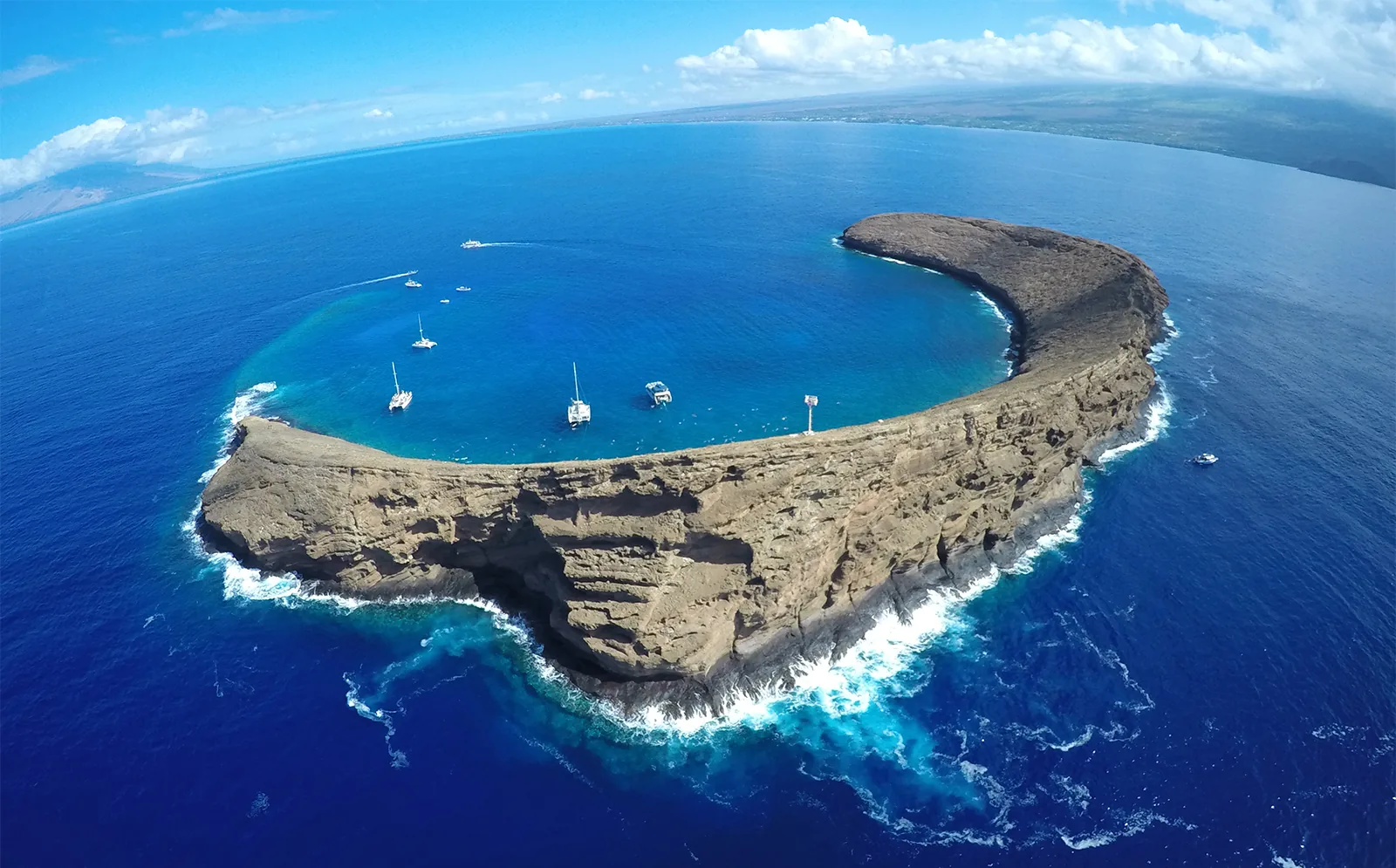 Aerial view of the crescent-shaped Molokini crater off Maui with snorkel boats moored inside