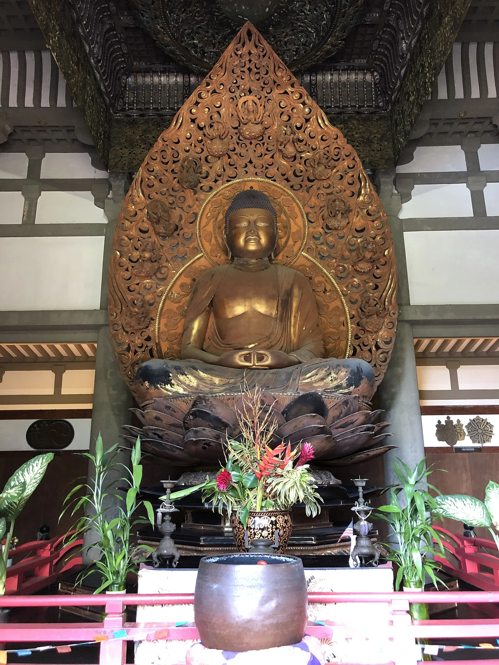 A large gilded seated Buddha statue in front of a carved golden halo inside the Byodo In Temple hall, with flowers on the altar
