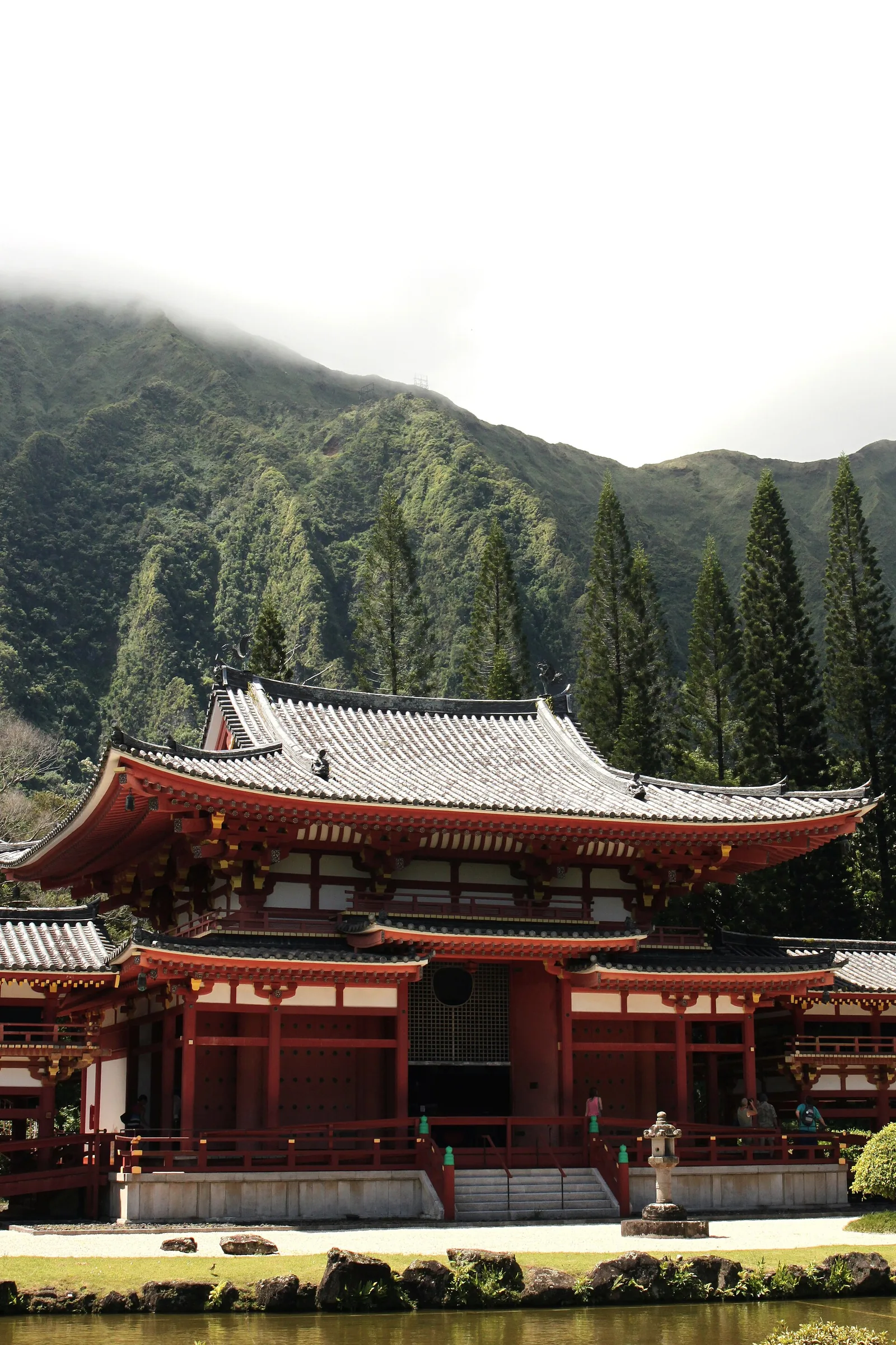 The red Byodo-In Temple roofline in front of misty green mountains and tall pine trees