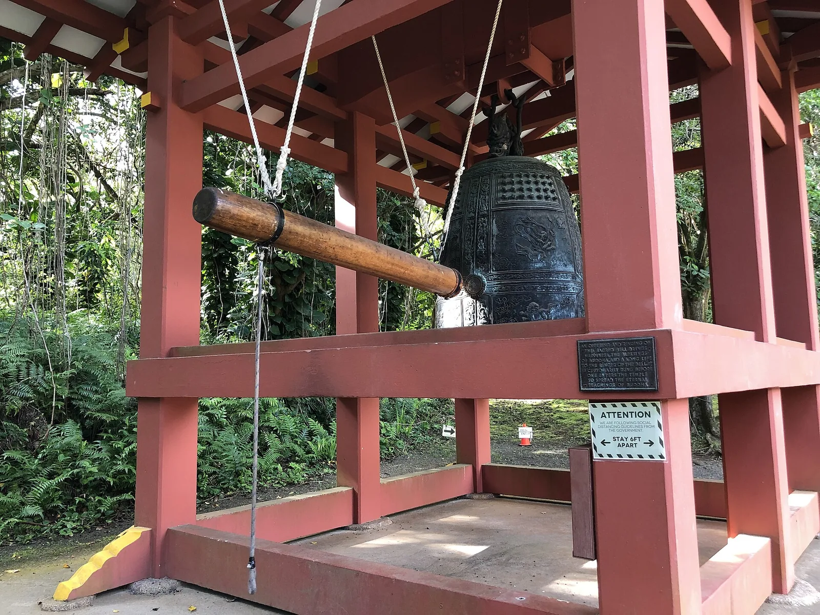 A large dark bronze temple bell with a horizontal wooden striking log hanging beside it in a red wooden frame
