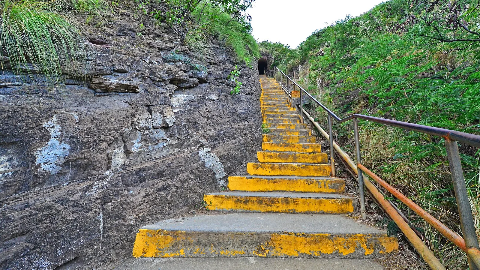 Concrete stairs with yellow-painted edges climbing towards the tunnel on the Diamond Head trail