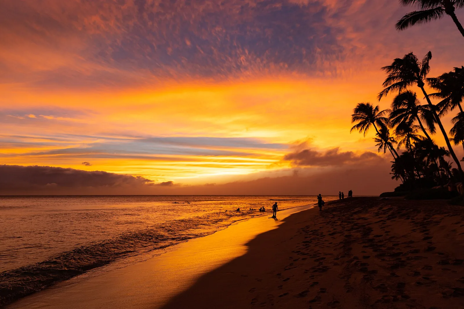 Orange sunset over Kaanapali Beach on Maui with palms and people walking the sand, a classic Hawaii honeymoon evening