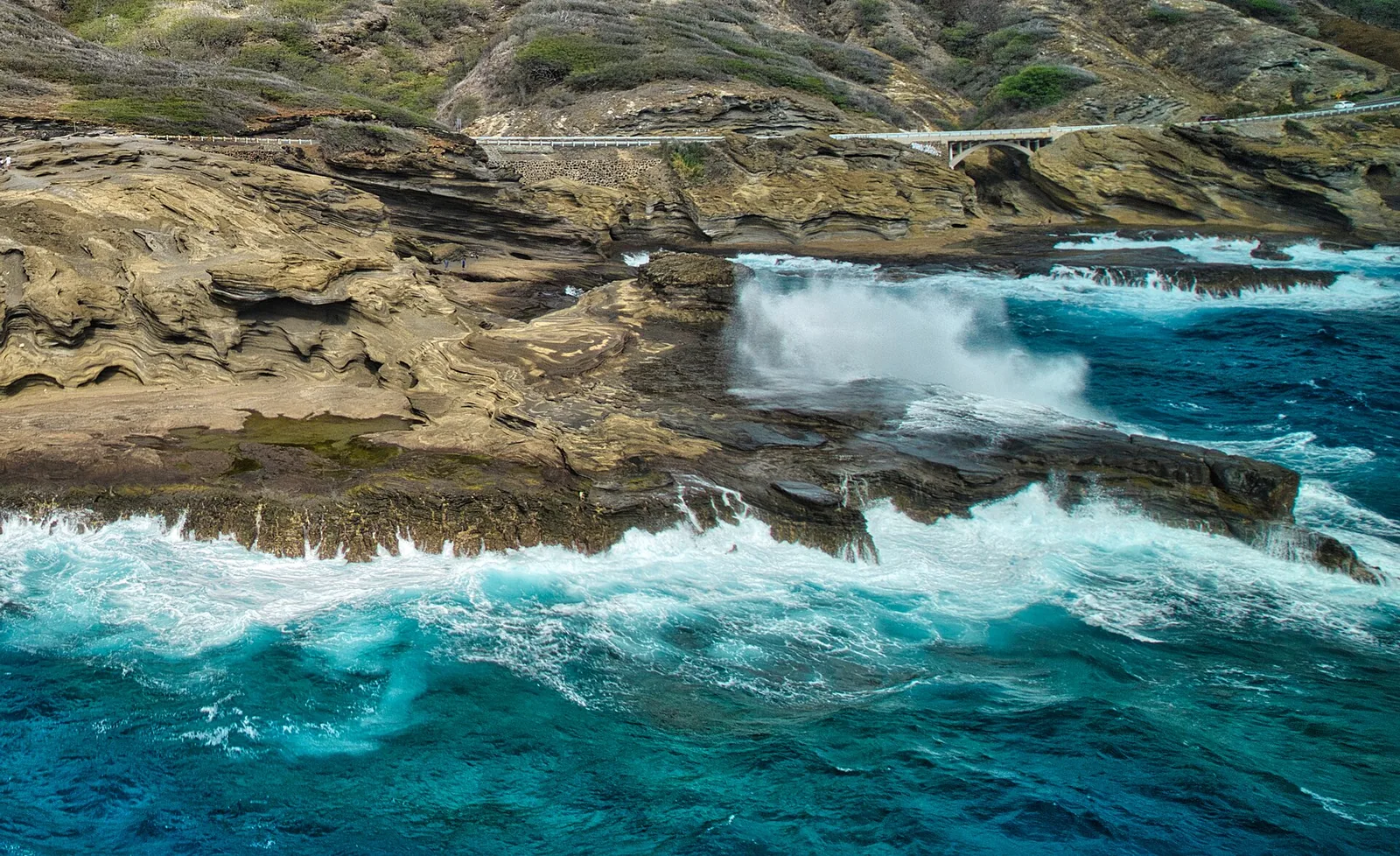 Waves crashing against the layered tuff cliffs at Lanai Lookout on Oahu's southeast coast